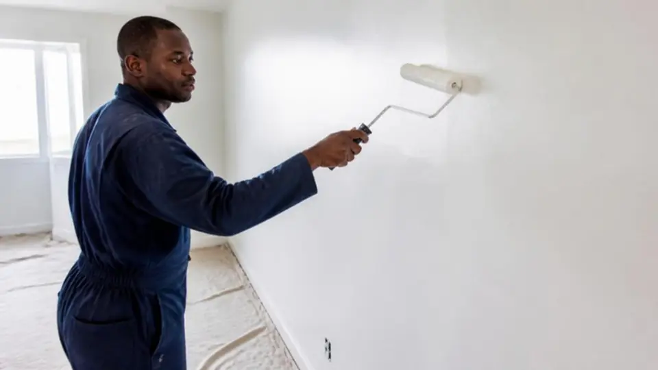 Pintor a aplicar tinta branca com rolo numa parede estucada